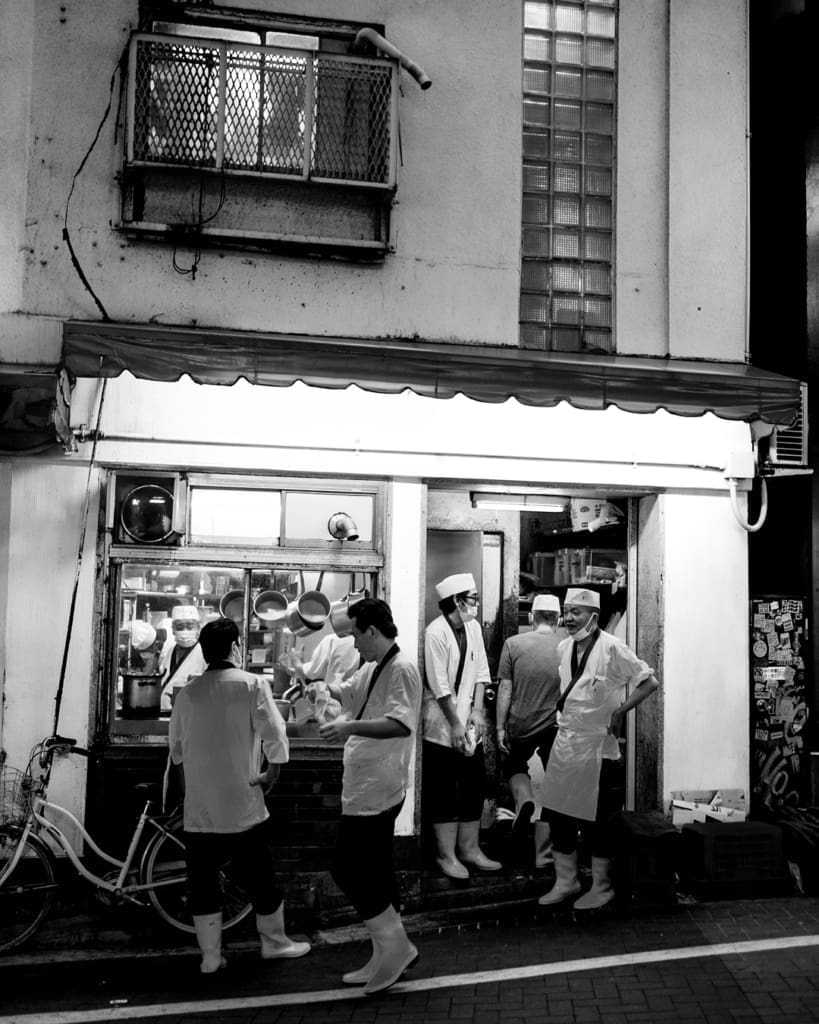 A black and white photo of a chefs outside a backstreet restaurant in Tokyo