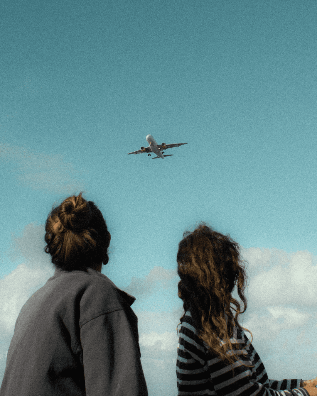 Two people look up at a plane in a blue sky, photography by Juan Goyache