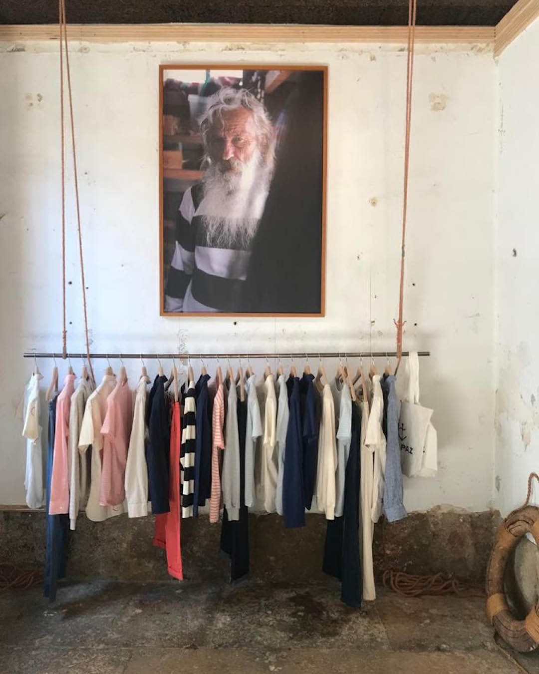 Clothes hang on a suspended rail beneath a portrait at La Paz shop in Lisbon.