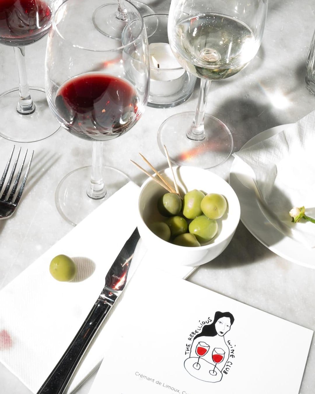 Red wine, olives and an illustrated menu decorates a table at The Rebellious Wine Club