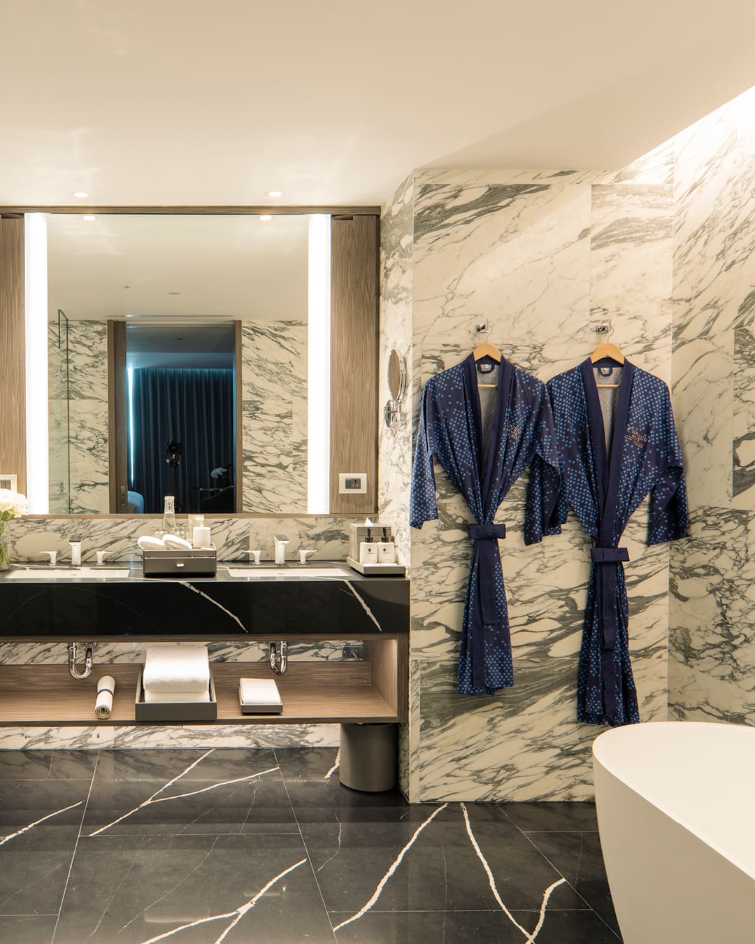 Luxury bathroom with mirror, hangomg robes and batch tub in a room at Chatrium Grand Bangkok