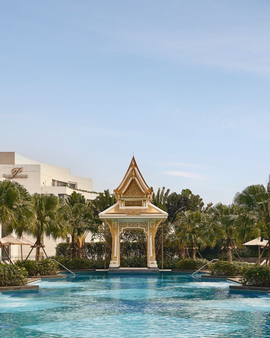 View of pool towards traditional Thai sala with trees and poolside lounges at Chatrium Grand Bangkok