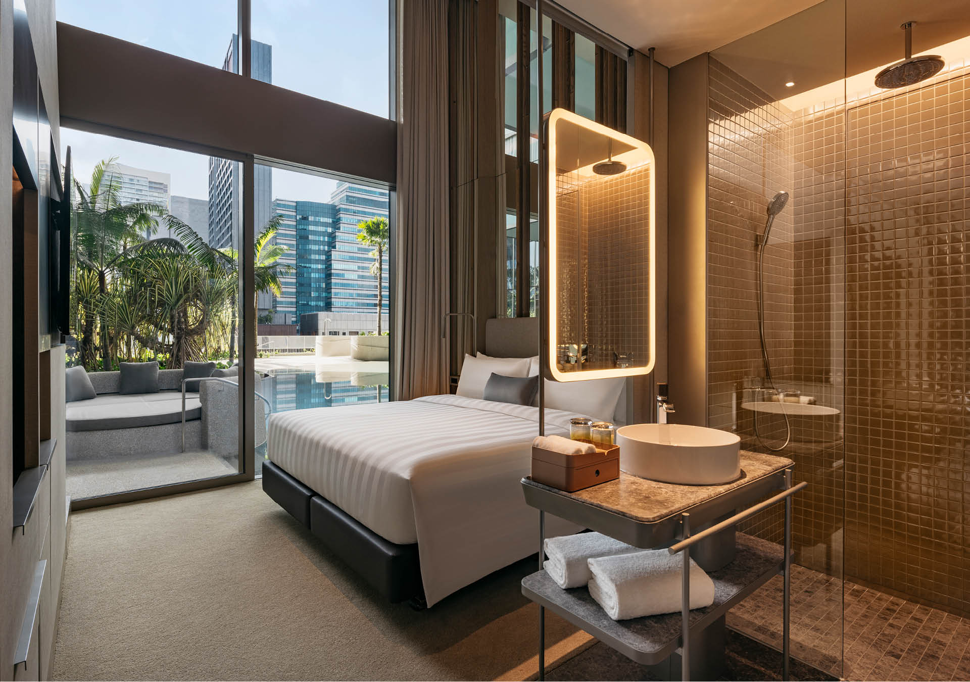 A loft room at Pan Pacific Orchard, with an ensuite shower visible through glass in the foreground, and a direct exit to a pool and patio in the background.