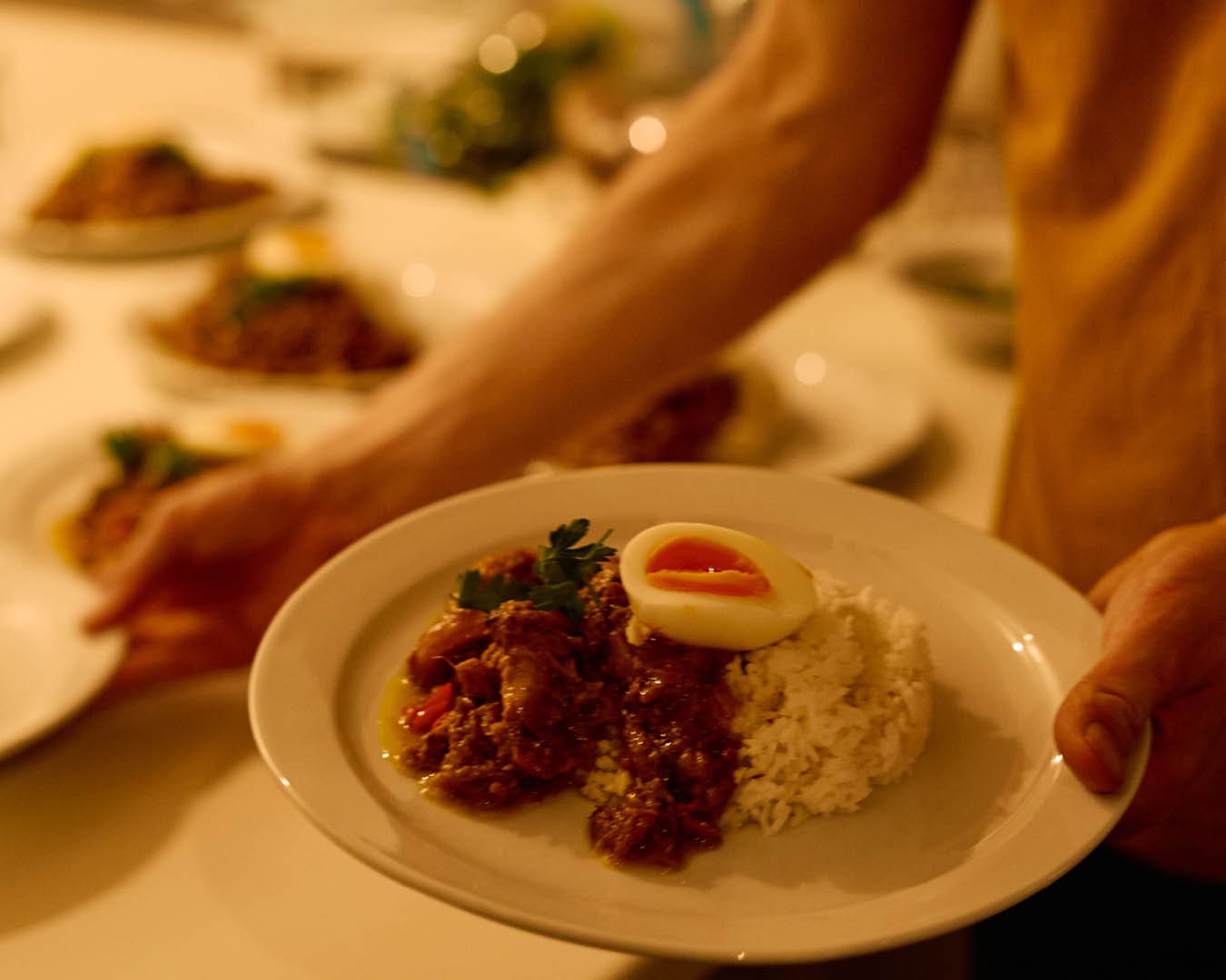 A chef carries freshly plated food over to a table at Alexander Does Supper Club