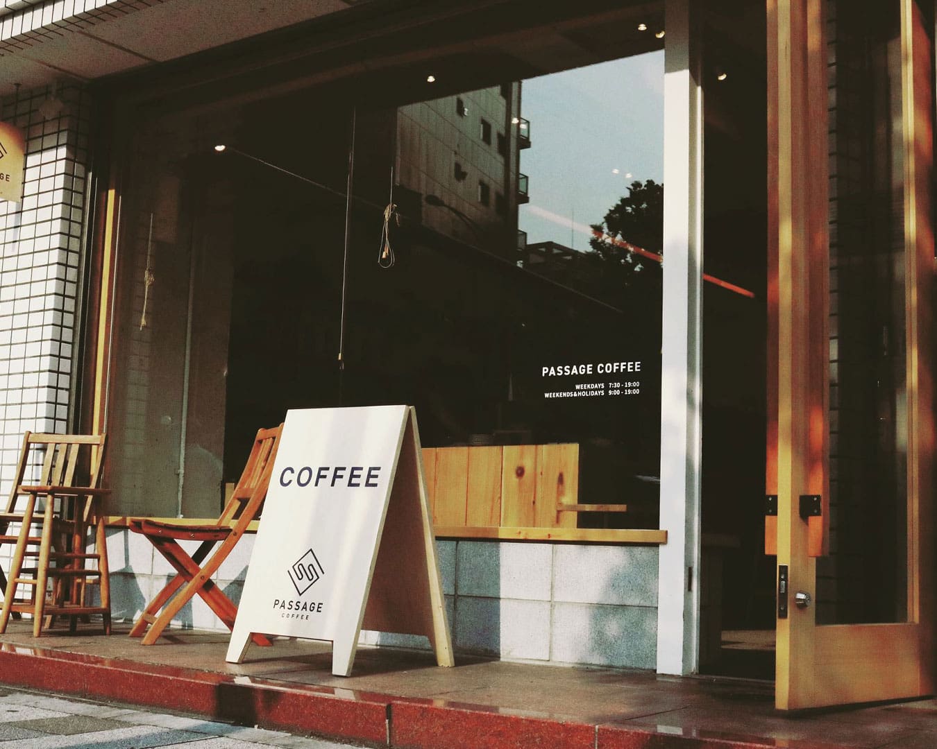 Outside Passage Coffee in Tokyo, a sign reading 'coffee' stands before a large window.