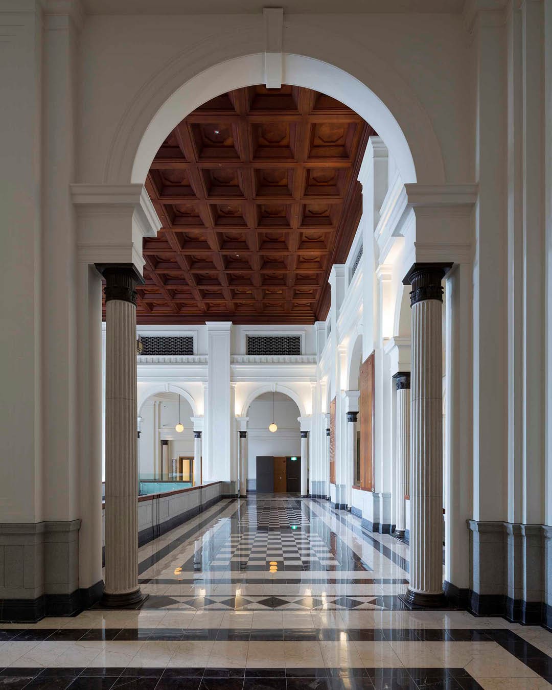 A colonnaded corridor with polished floors and a tiled ceiling in National Gallery Singapore