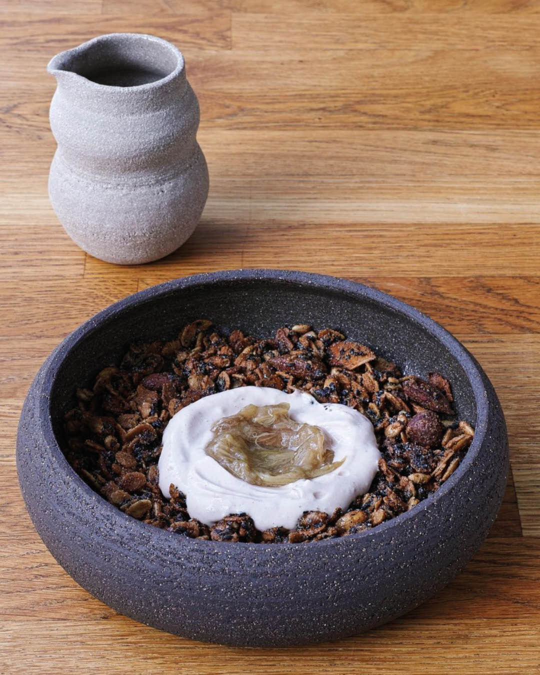 A granola bowl served in a charcoal grey ceramic bowl with a small grey ceramic jug at Fringe coffee shop in Paris.