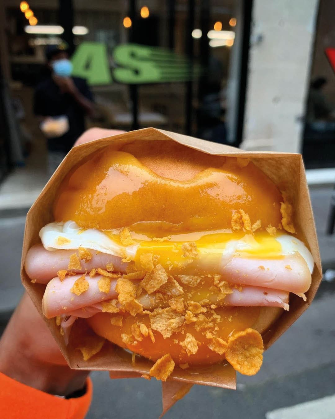 A ham, egg and cheese cereal bunheld in a brown paper bag outside Paperboy coffee shop in Paris.