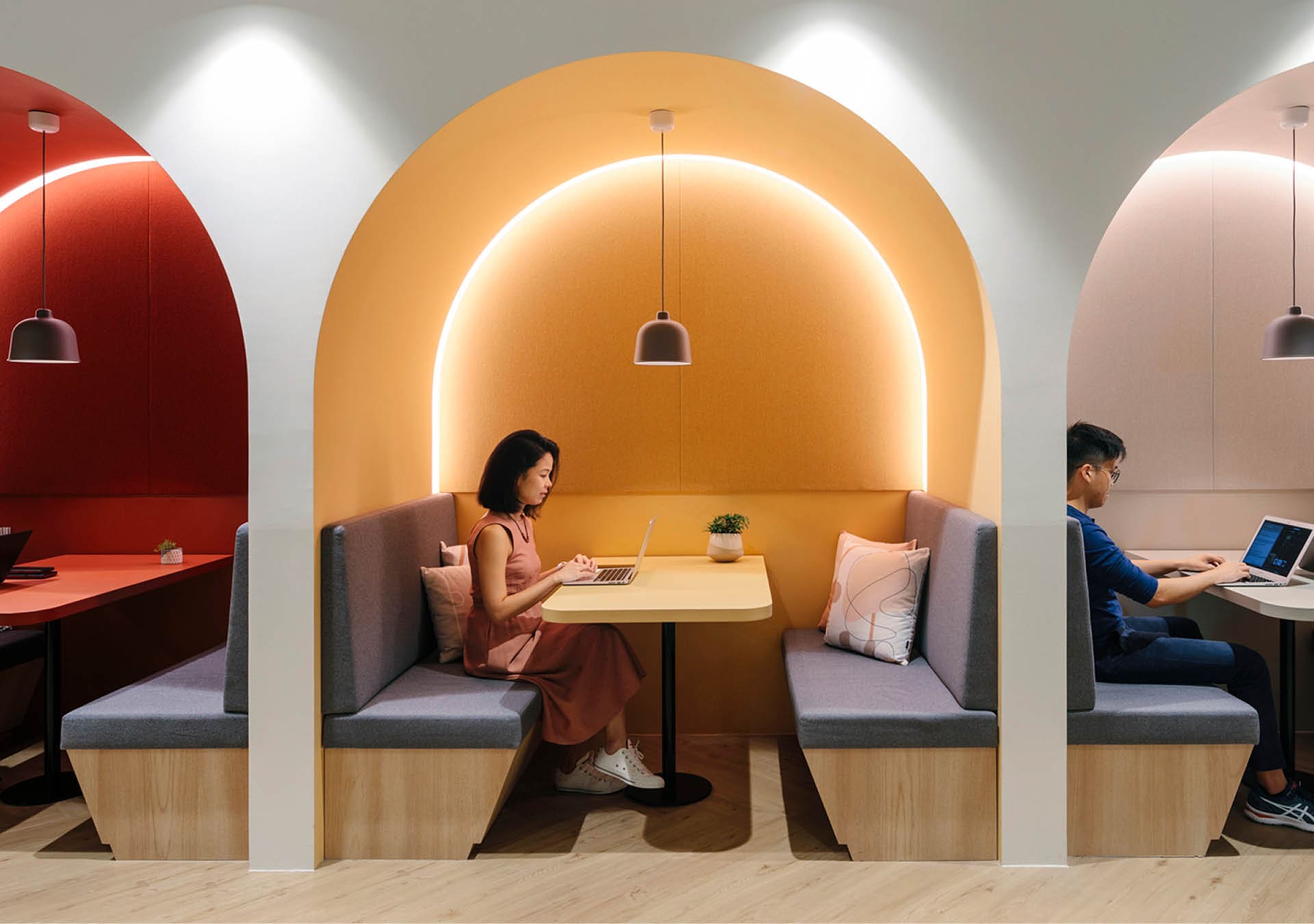Private booths with people working at desks at JustCo, Centrepoint, underneath colourful arched ceilings.