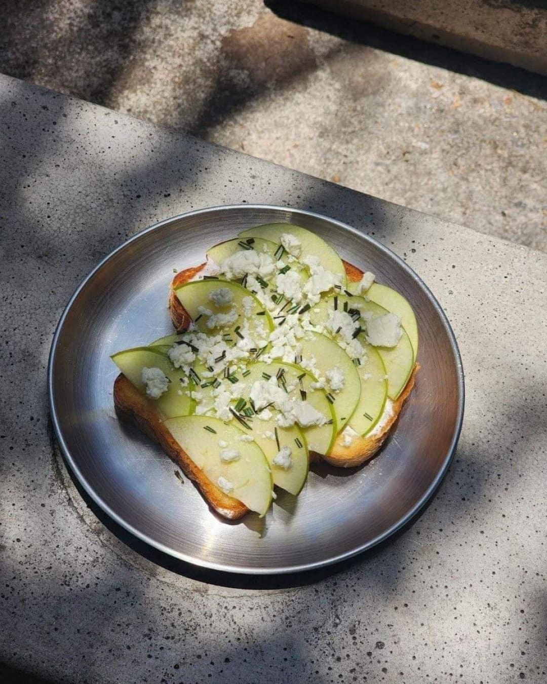 Open toast with slices of apple, served on a zinc table at Karo Coffee Roasters.