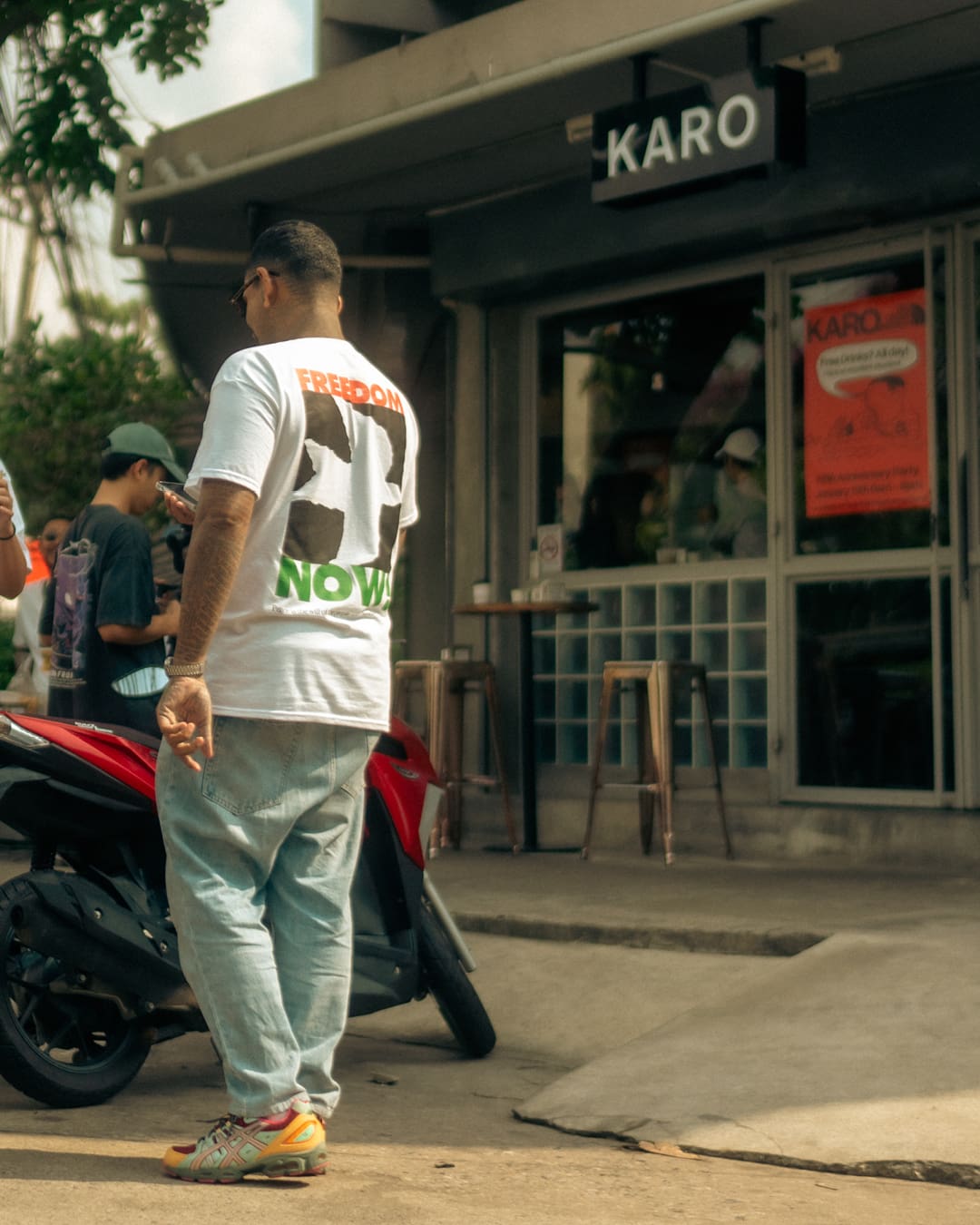 Karo standing outside Karo Coffee Roasters next to a red scooter.