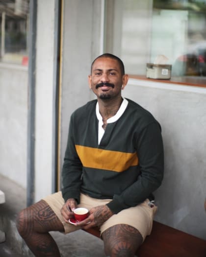 Karo Lyash, sat outside Karo Coffee Roasters, holding a red coffee cup in his hands.
