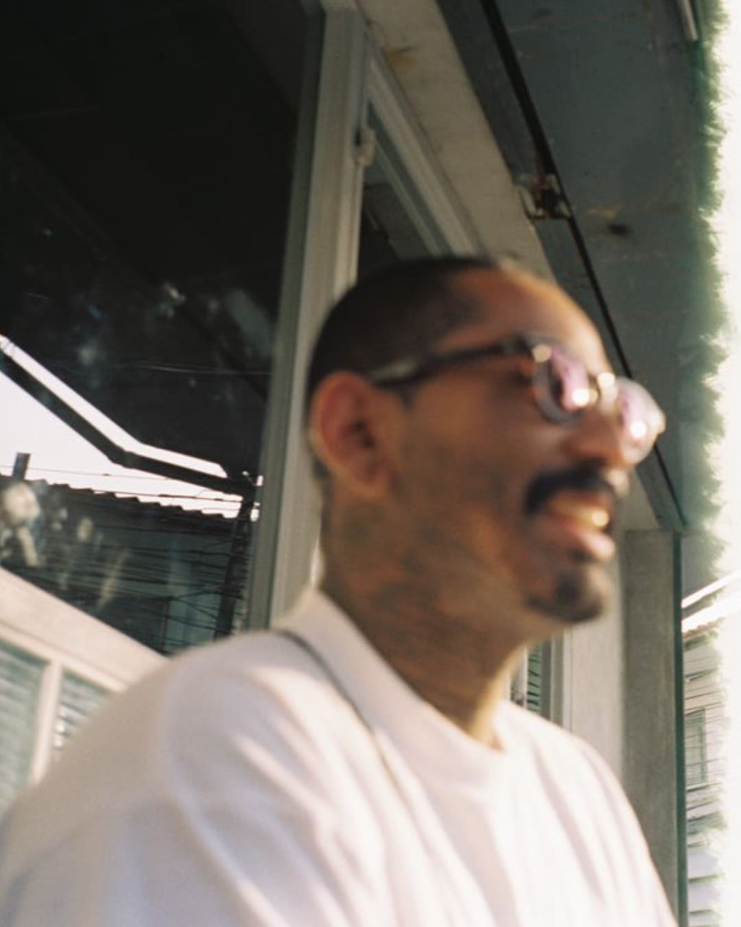 Karo Iyash wearing a white t-shirt and sunglasses, captured on film.