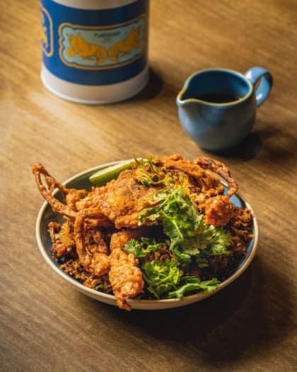 Soft shell crab served in a bowl on a wooden tabletop next to a small blue jug, at Kotuwa restaurant in Singapore.