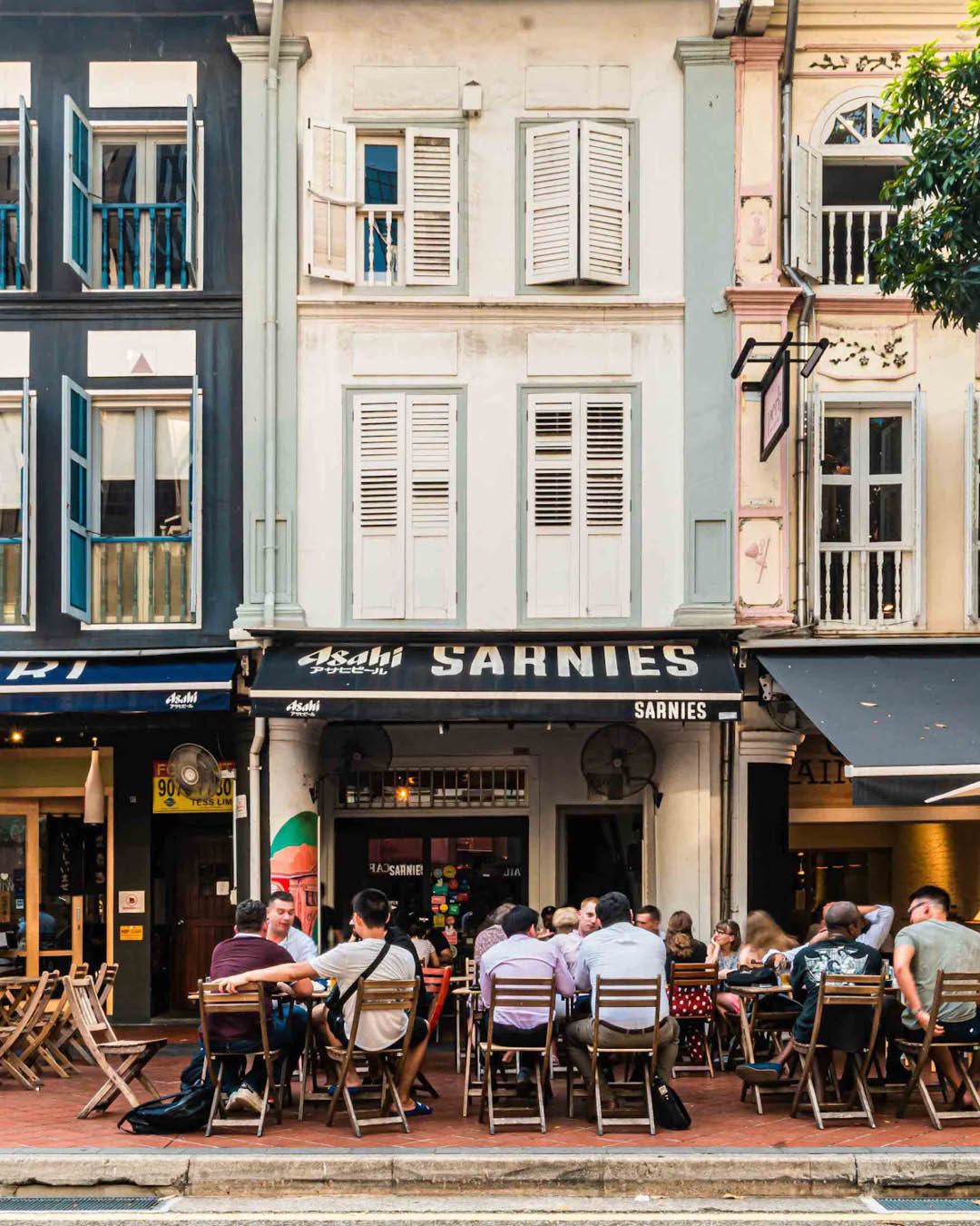People sit outside Sarnies cafe in Singapore on outdoor tables and chairs