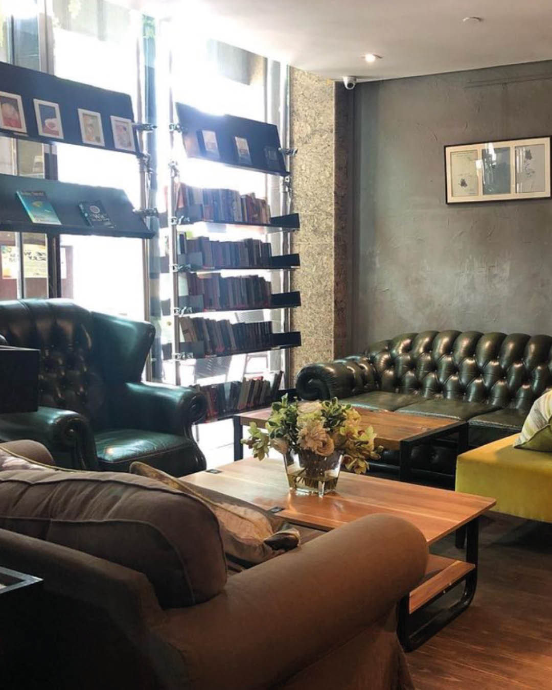A chesterfield sofa and two arm chairs around a wooden coffee table with book shelves nearby at The Book Cafe, Singapore.