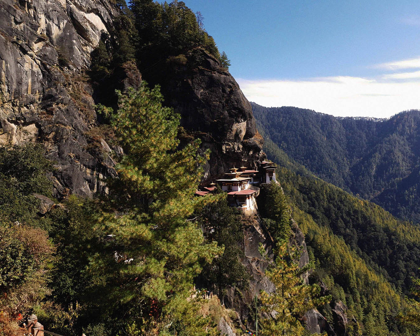 A breathtaking mountain landscape featuring a cliffside monastery nestled against a steep rock face.