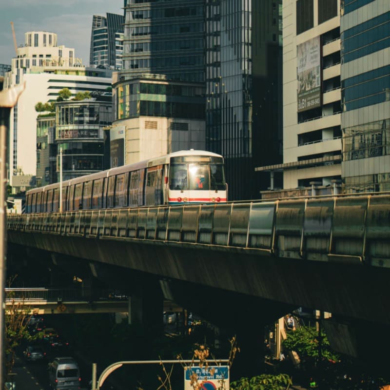 bts skytrain driving into sun next to city buildings in Bangkok