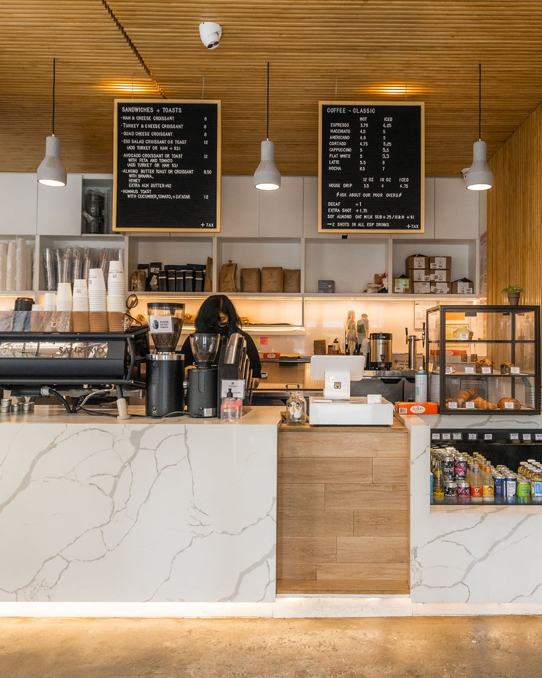 The marble and wood counter at Coffee Project New York with blackboards and shelving behind, and a coffee machine, till and various food on top.