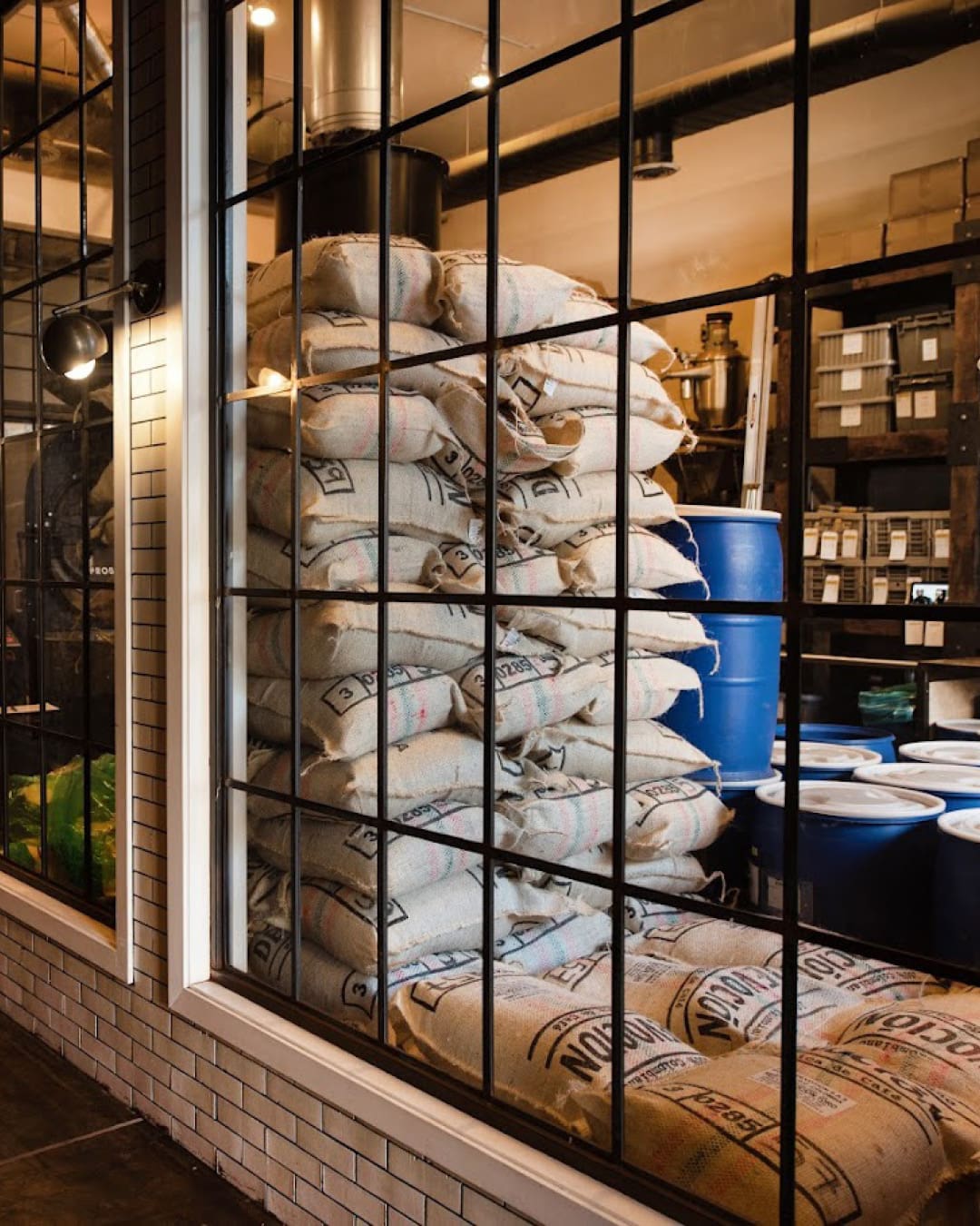Bags of coffee beans stacked at Devoción roastery in New York behind crittal windows.