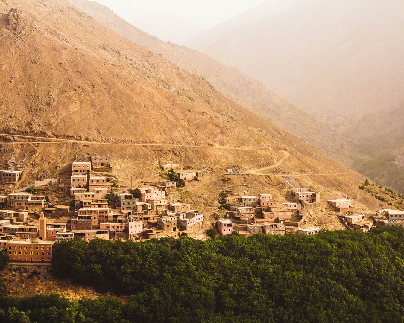 The mountainous village of Imlil in the Atlas Mountains. Small stone buildings sit on a rising hill above trees.