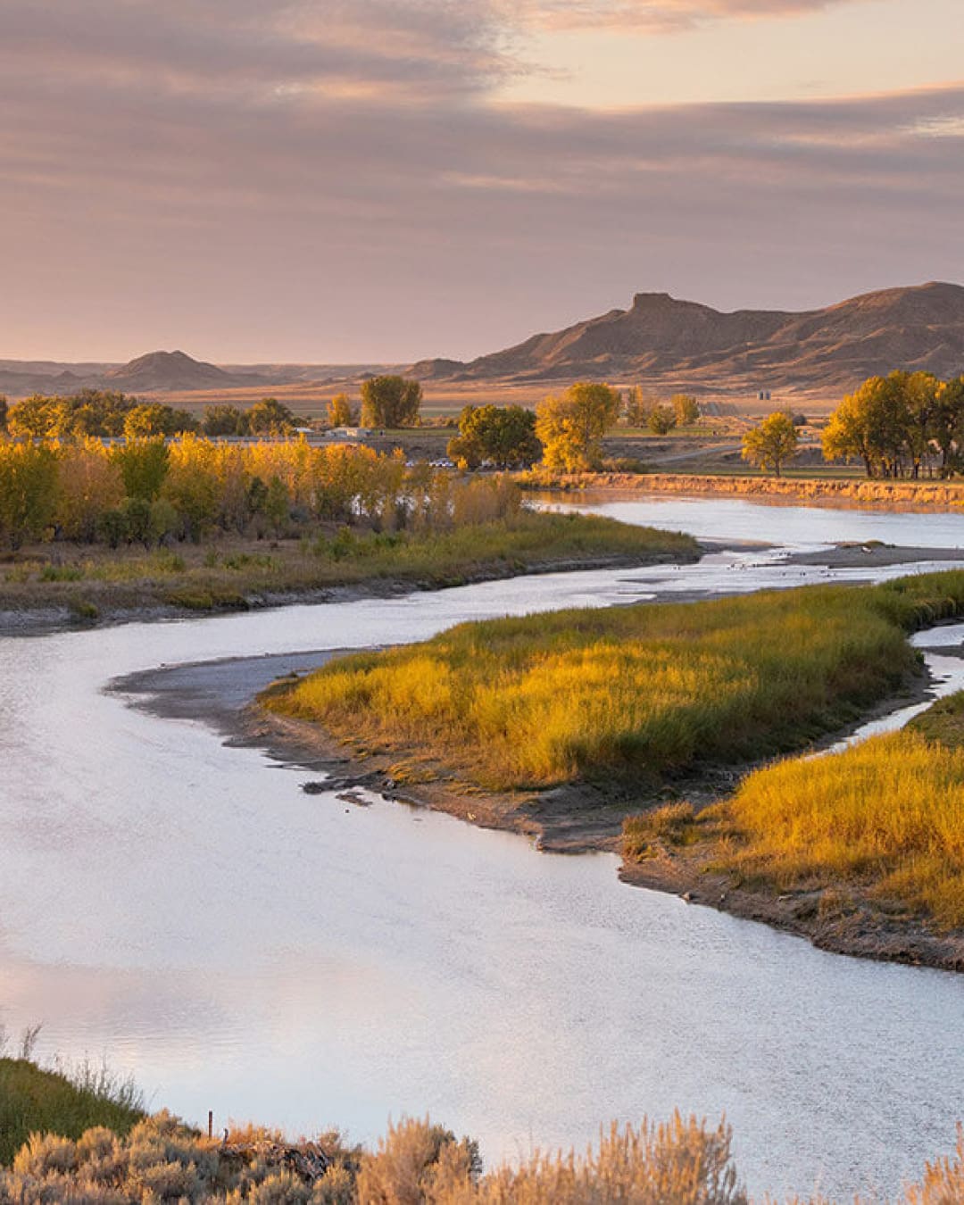 A river meanders through American Prairie nature reserve in Montana, US, at sunset.