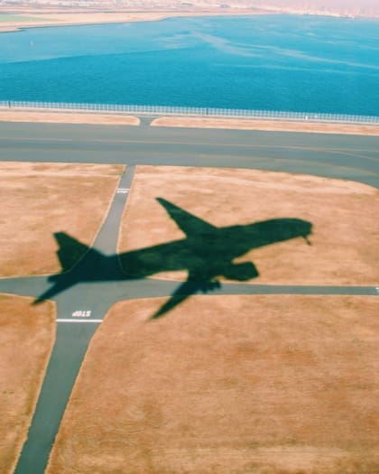 Shadow of an airplane flying over a runway with a scenic view in the background.