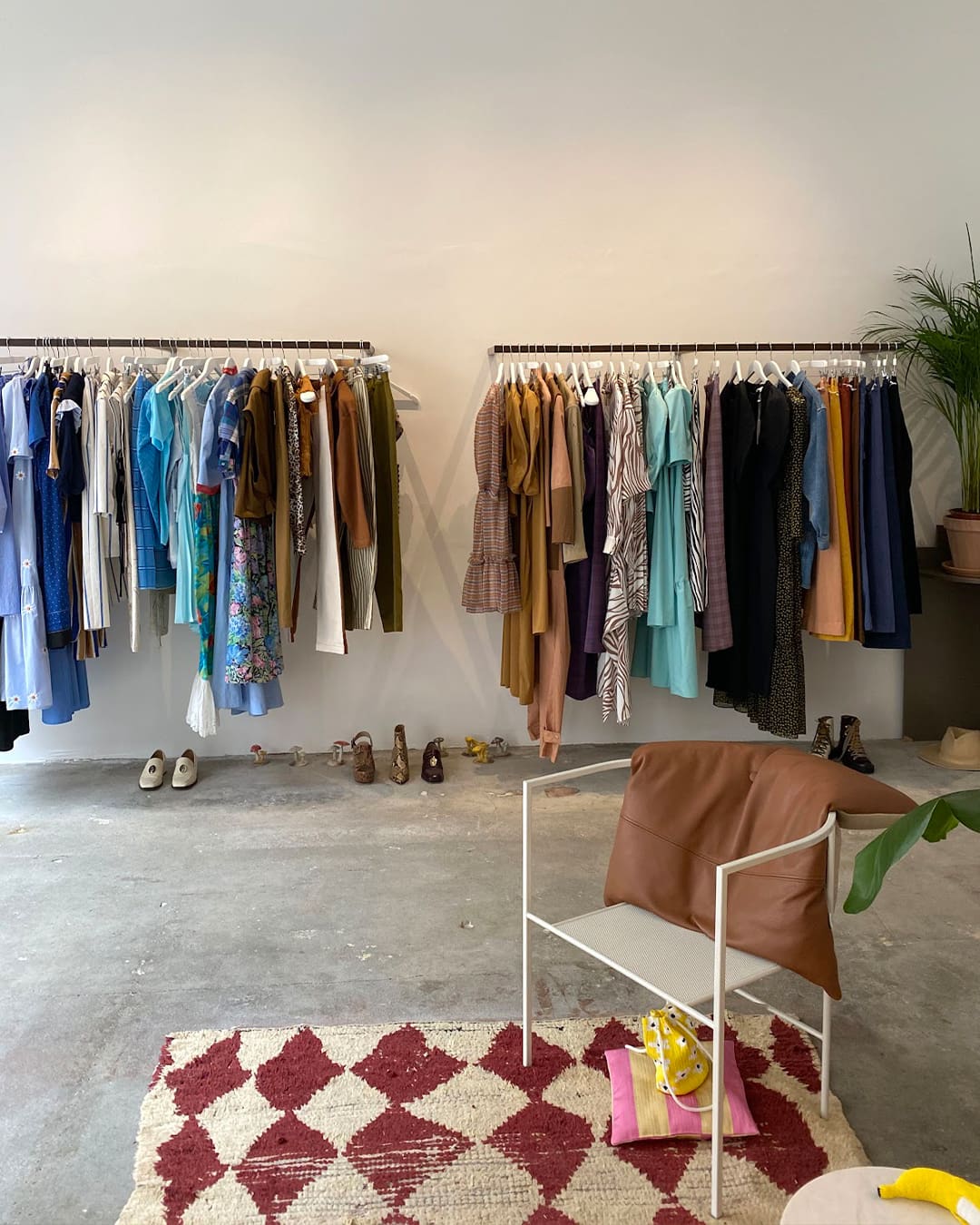 A metal armchair on a chequered red and white rug in the centre of a room with two clothes rails behind along a white wall, in Mr Larkin clothes shop in Copenhagen.