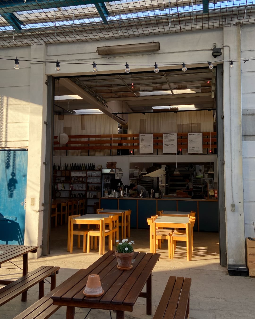 The courtyard at Flere Fugle bakery, where wooden tables sit inside and out of a former garage that now houses the bakery and pizza bar.