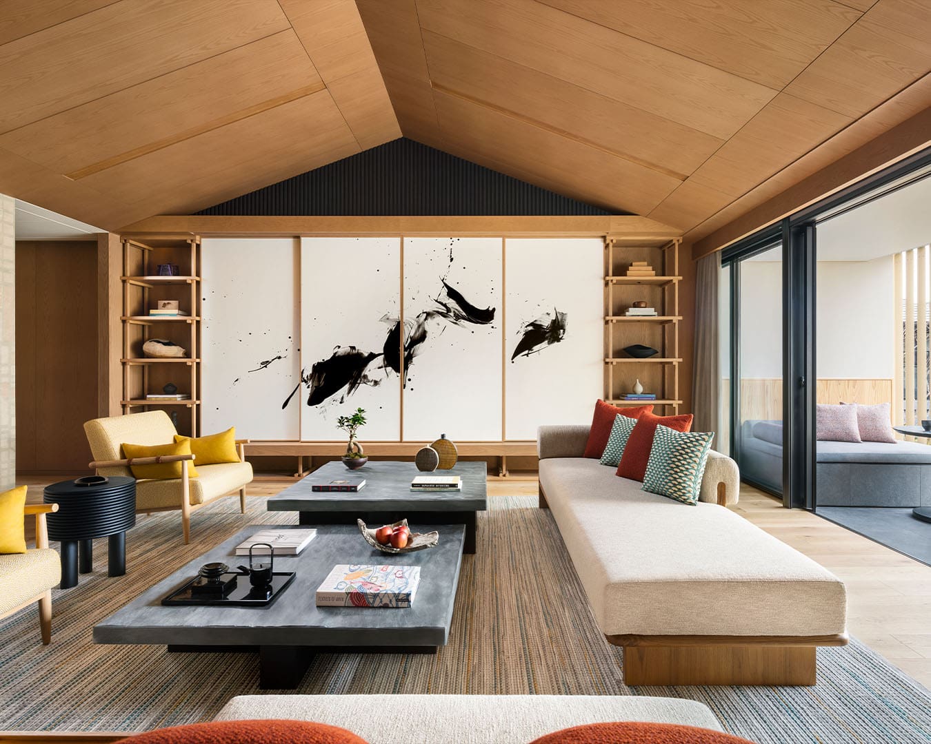 The living room in Six Senses Kyoto's three-bedroom penthouse, where white sofas and arm chairs surround a low black table and a black and white abstract painting hangs on the wall below a pitched ceiling.