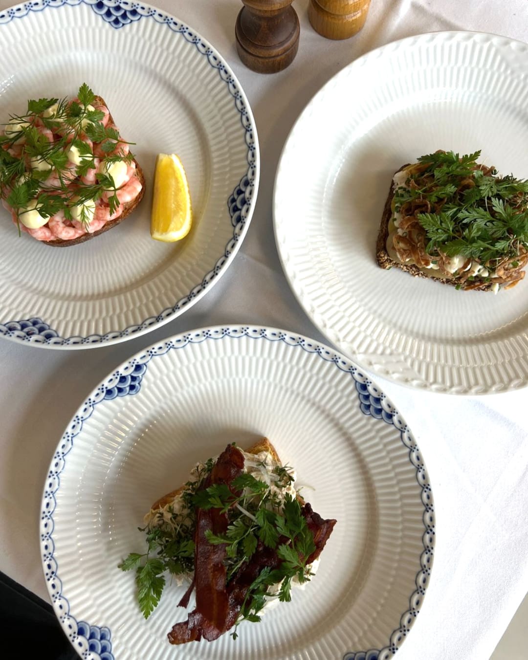 Three white plates with different smørrebrød options on a white tablecloth at Lumskebugten restaurant in Copenhagen.