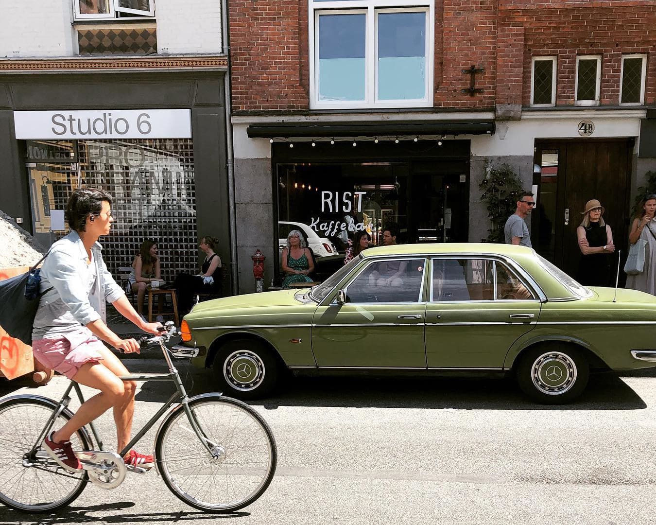 A green car parked outside Rist cafe and bar in Copenhagen, while a cyclist cycles past.