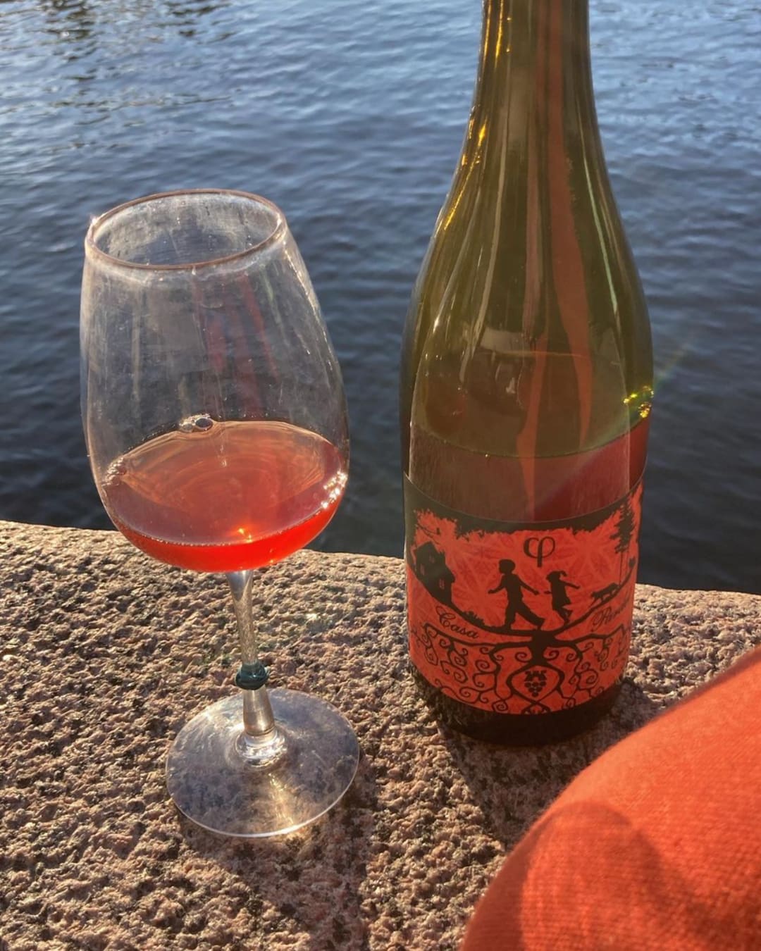 A bottle of orange wine and a glass on the edge of the water in Copenhagen K