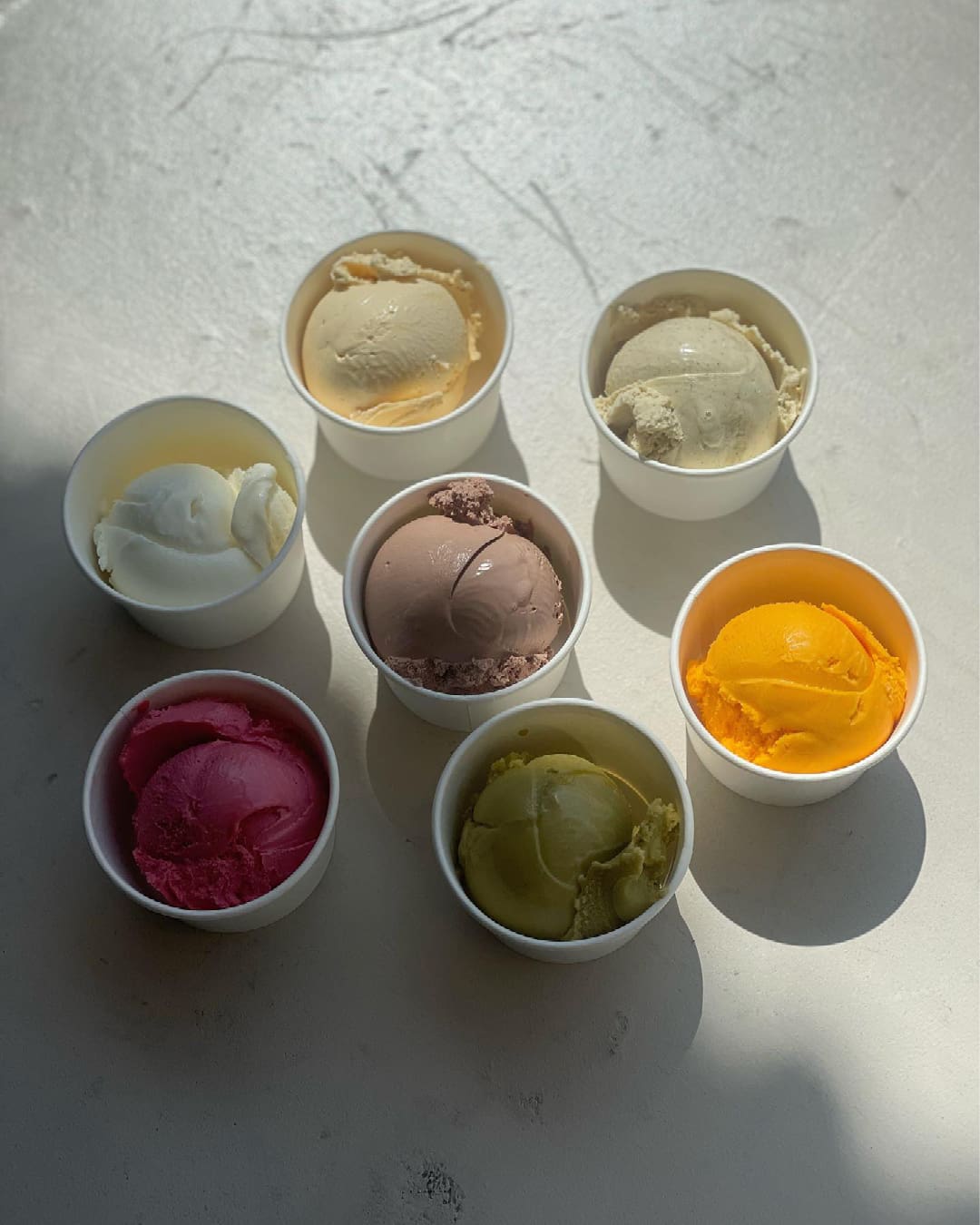 An assortment of ice cream flavours at Alice Ice Cream & Coffee, each one a single ball in a white cup.