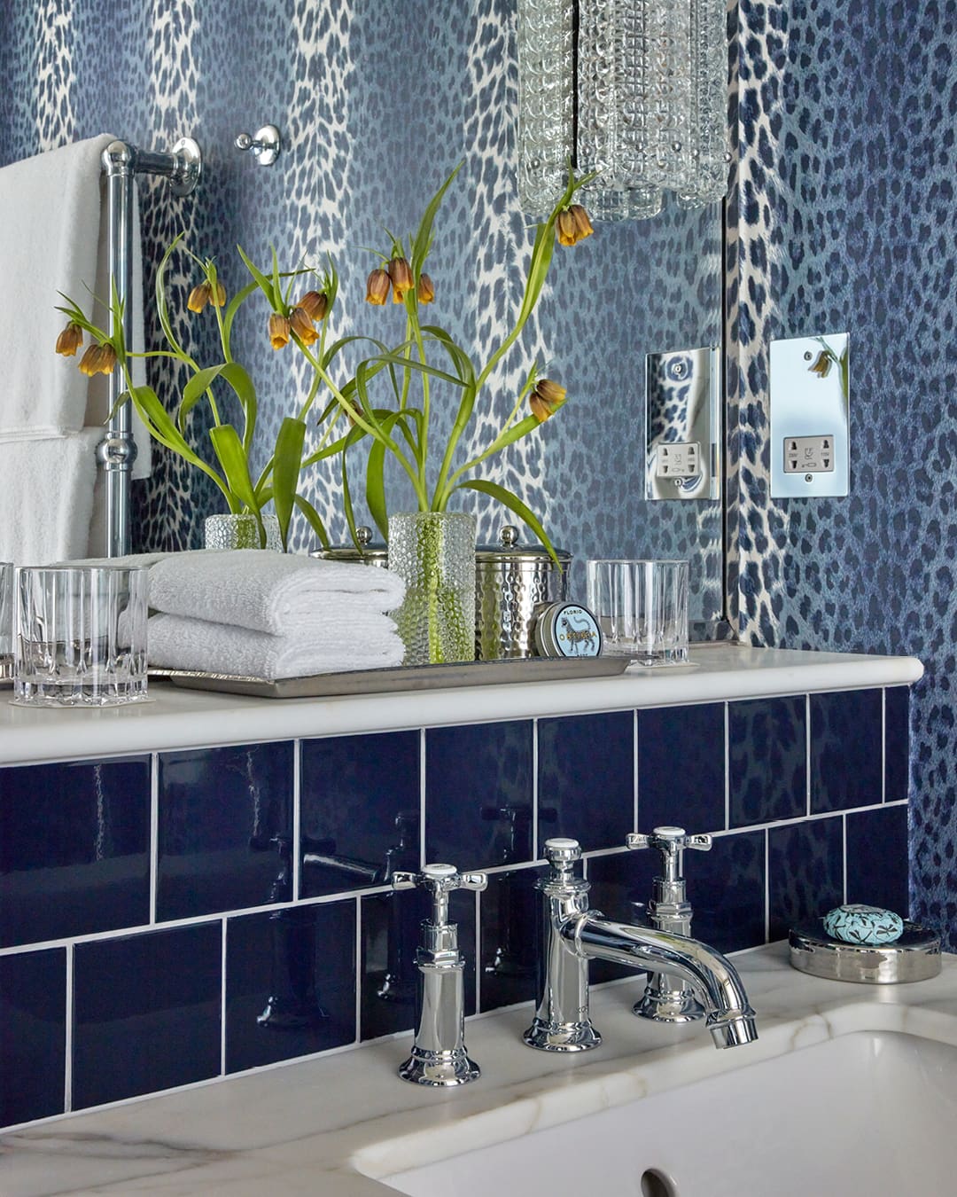 Stylish blue bathroom at Broadwick Soho, London, featuring fresh flowers, luxurious toiletries, and elegant fixtures against a patterned wall.