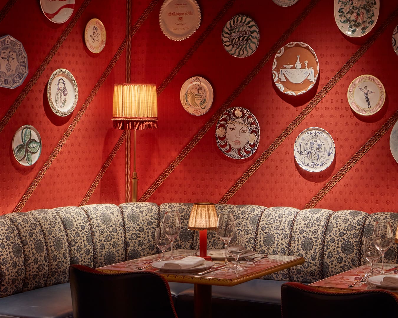 Charming interiors at restaurant Dear Jackie, featuring a cozy banquette, decorative plates on a vibrant red wall, and elegant table settings.