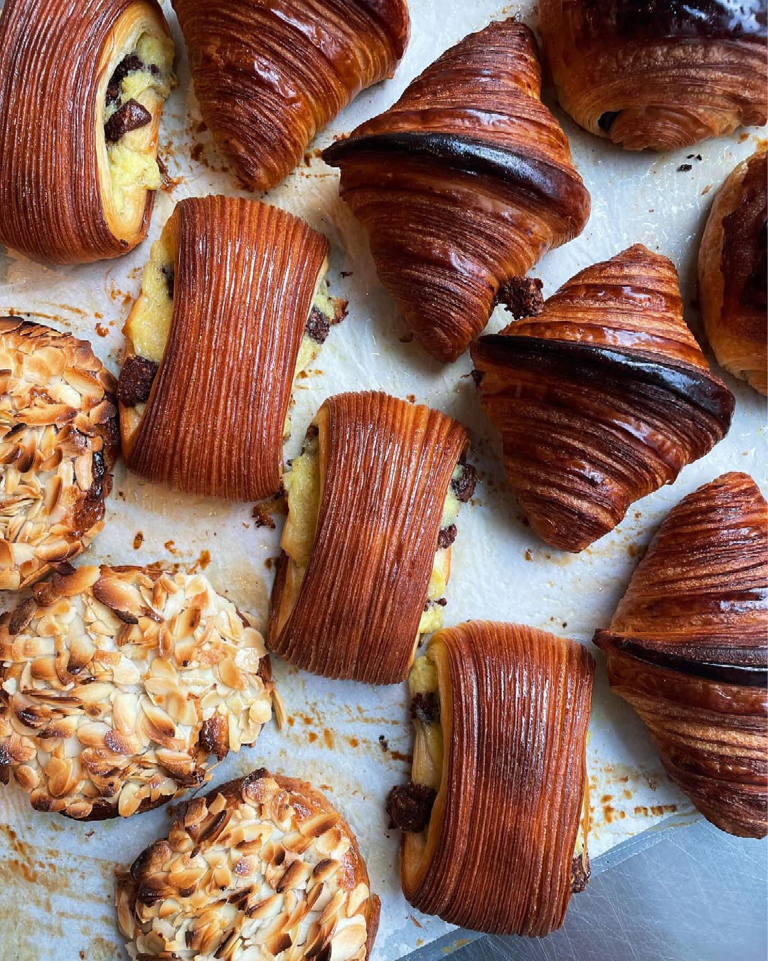 Crispy laminated pain Suisse filled with chocolate and vanilla custard on baking paper next to croissants and almond baked goods at Juno Bakery in Copenhagen.