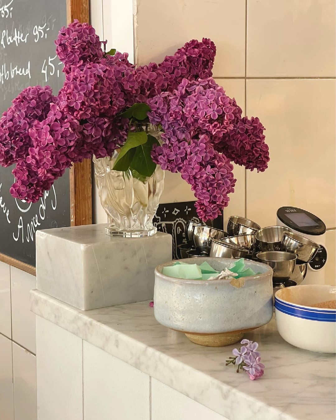 Lilacs displayed in a glass vase on a marble counter at Atelier September cafe in Copenhagen next to two bowls and a collection of coffee filters.