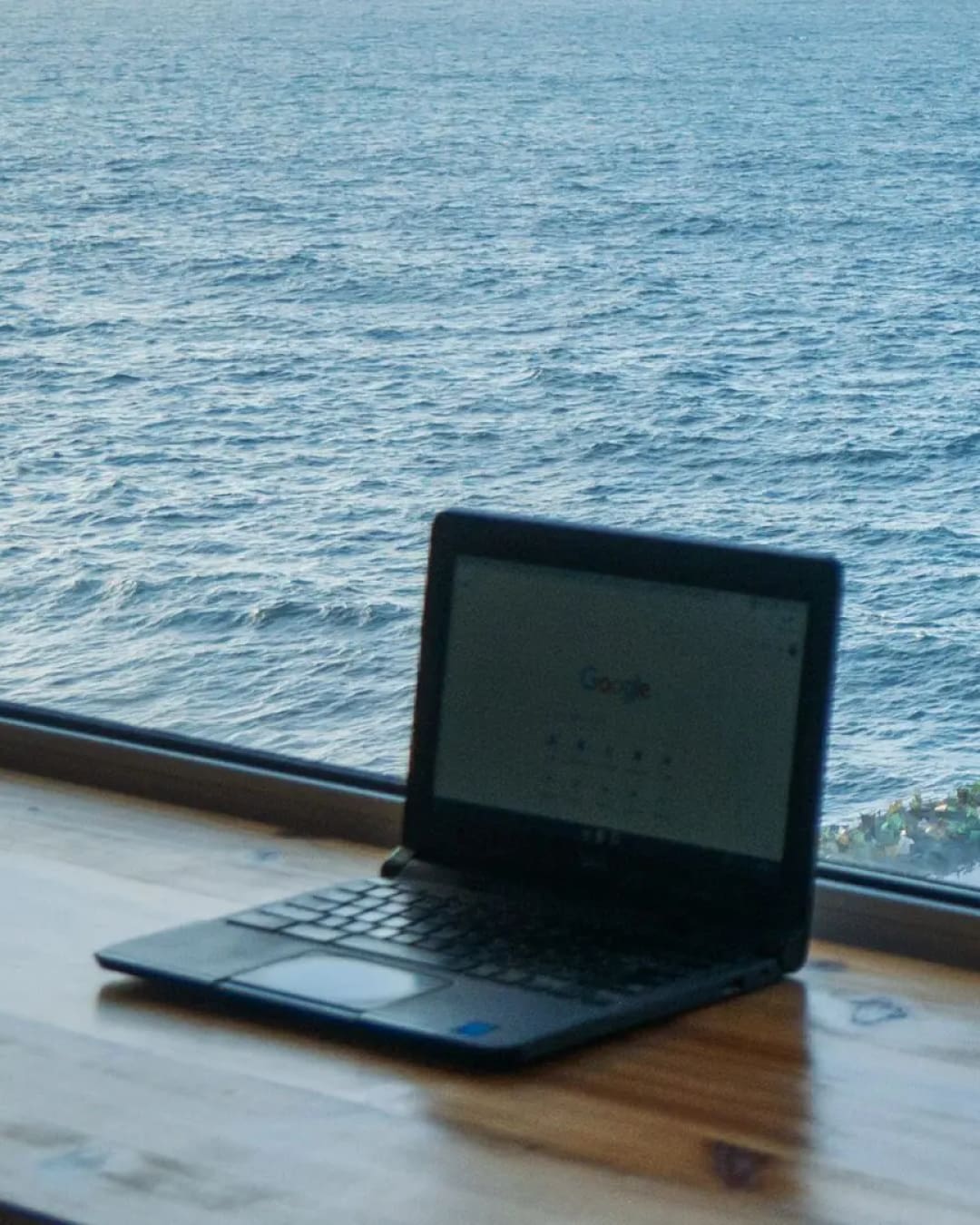 Open laptop on a wooden table with a view of the ocean in the background, ideal for remote work or digital nomad lifestyle