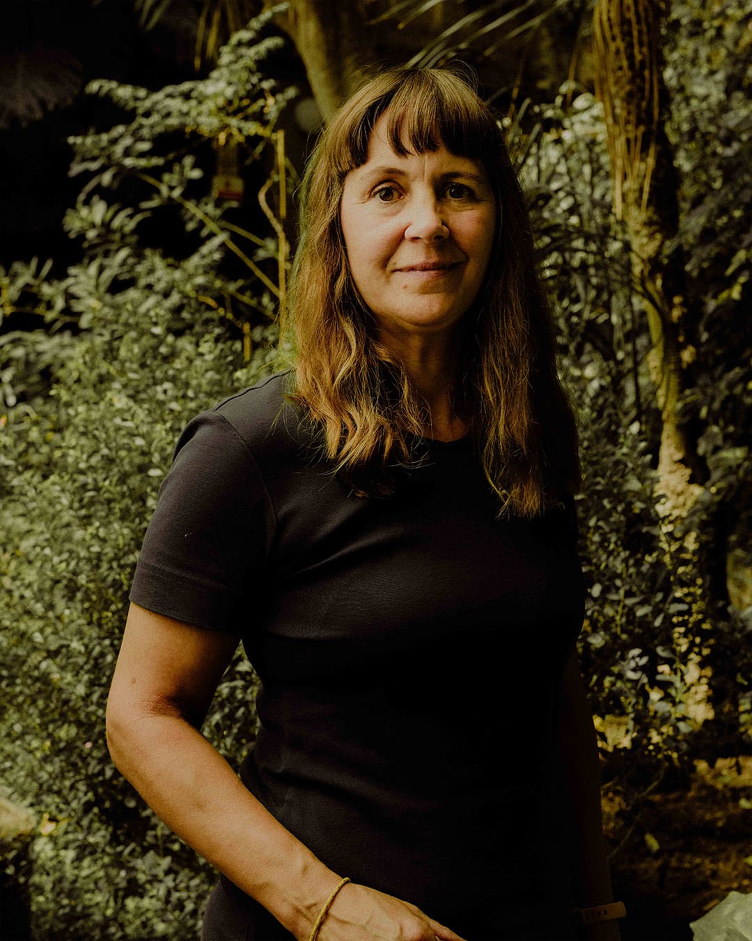 A portrait of gardener Sara Fox against a backdrop of shurbs.