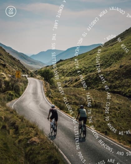 Cycling through the Elan Valley, with text overlaid on top of the image of two cyclists pedalling down a narrow lane between two green hills, with mountains in the distance.