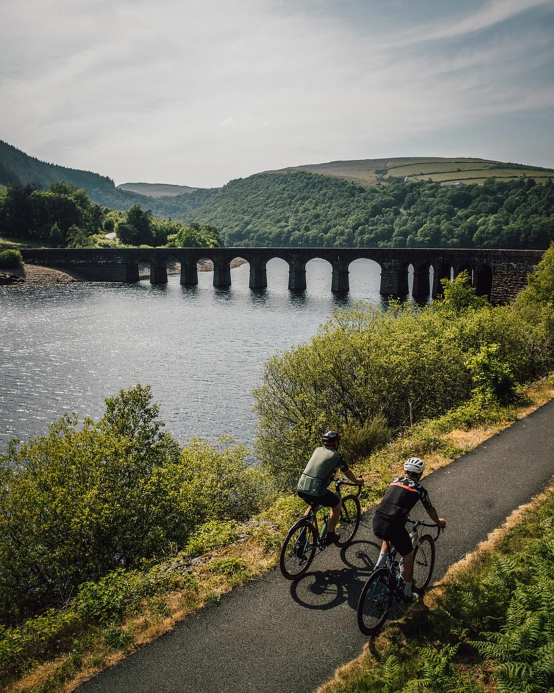 Two cyclists approach Garreg-Ddu Dam, with an aqueduct in the distance.