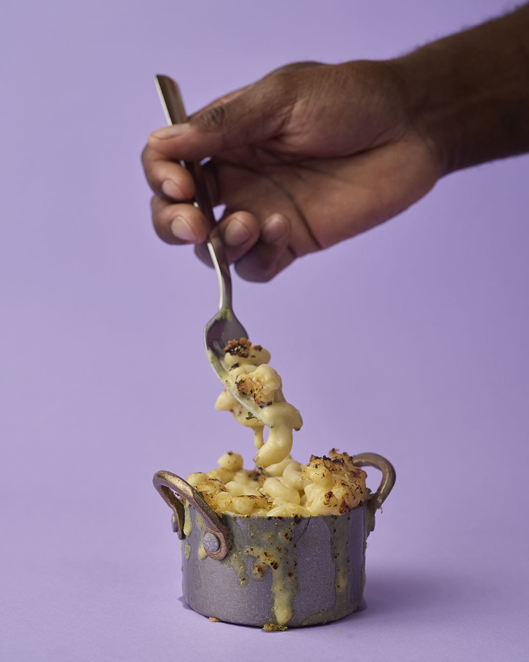 A hand serving Marvees delicious mac and cheese dish on a purple backdrop