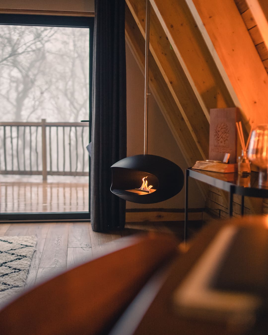 A modern floating log burner is lit inside a wooden treehouse.