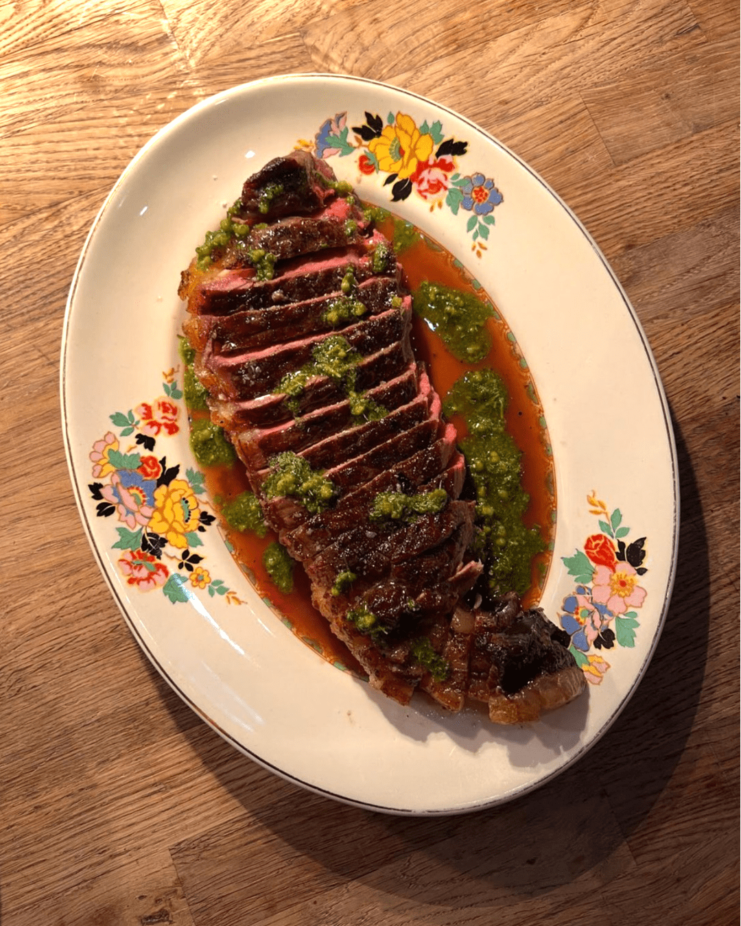 Succulent meat dish served on a floral plate at Coombeshead Farm, Cornwall, featuring sliced meat drizzled with vibrant green sauce.