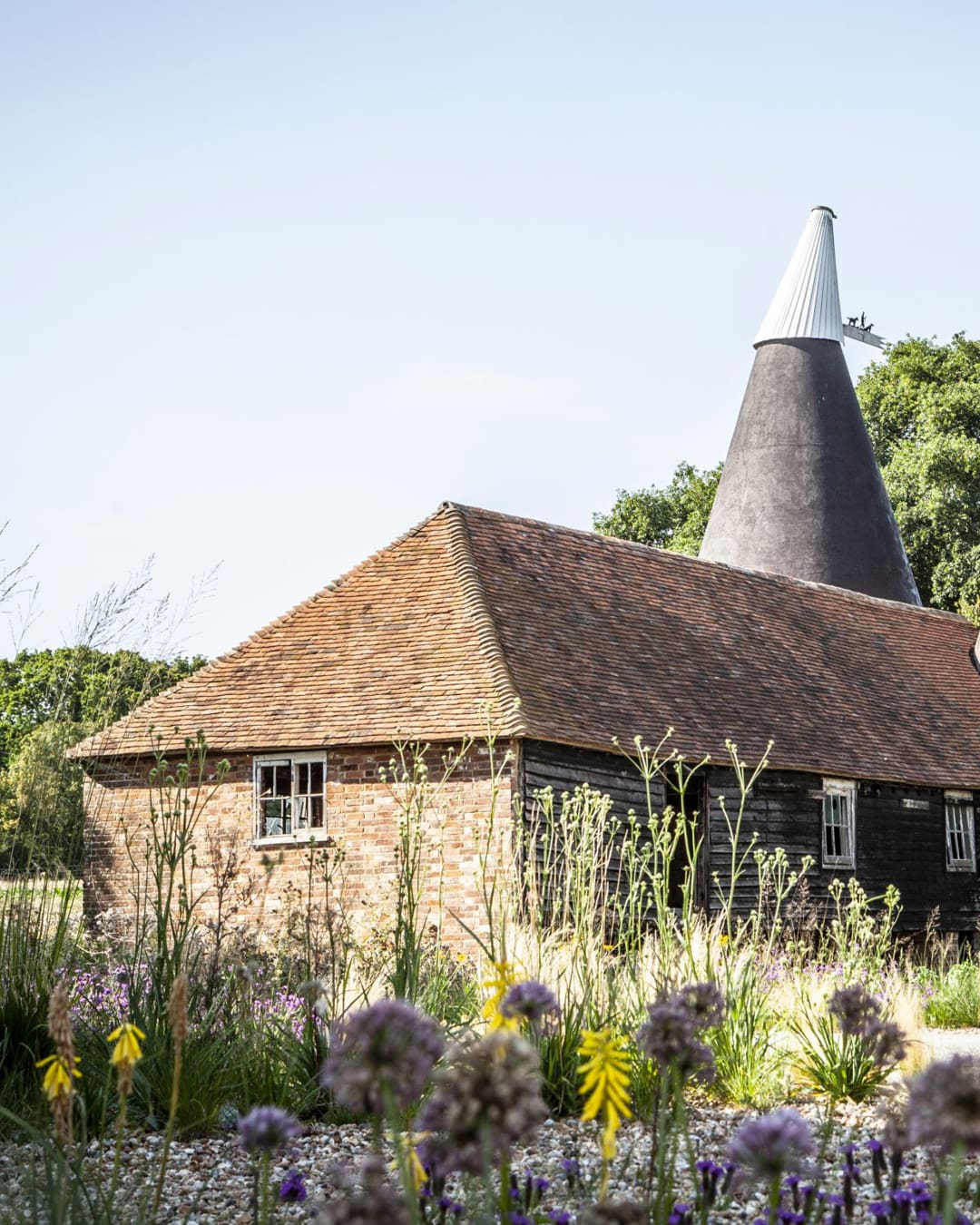 Charming Tillingham winery farmhouse in the UK, featuring a distinctive chimney and surrounded by vibrant wildflowers and lush greenery.