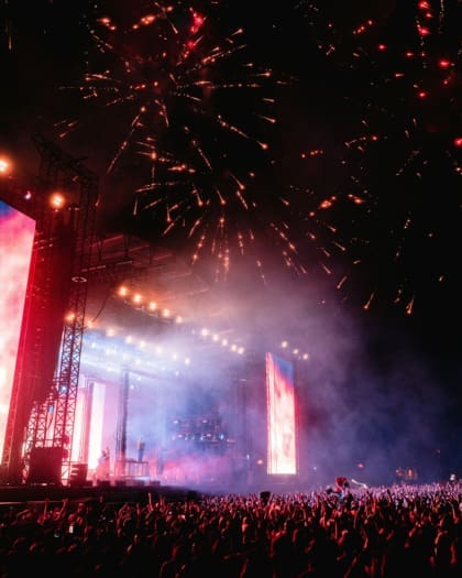 Crowds dance beneath a display of fireworks at a music festival