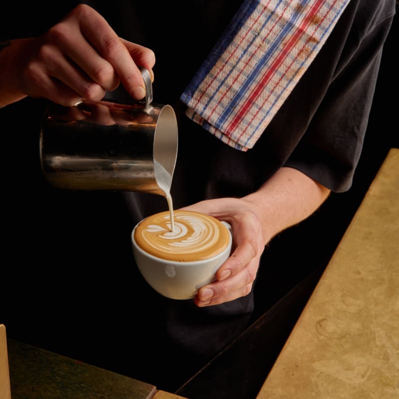 Barista making a cappucino with coffee art at Square One cafe in Melbourne.