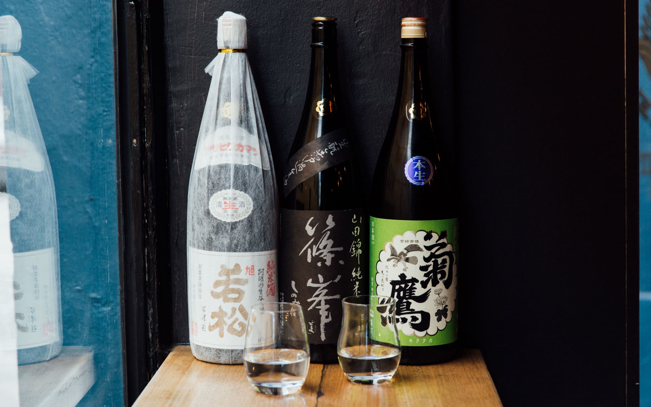 Three bottles on a table at Tamura Sake Bar, with two glasses