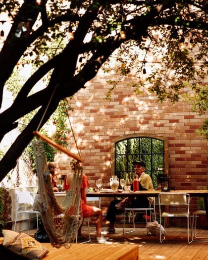 People sitting in sun dappled backyard drinking wine and talking at Sauced, a wine bar in New York City, NYC
